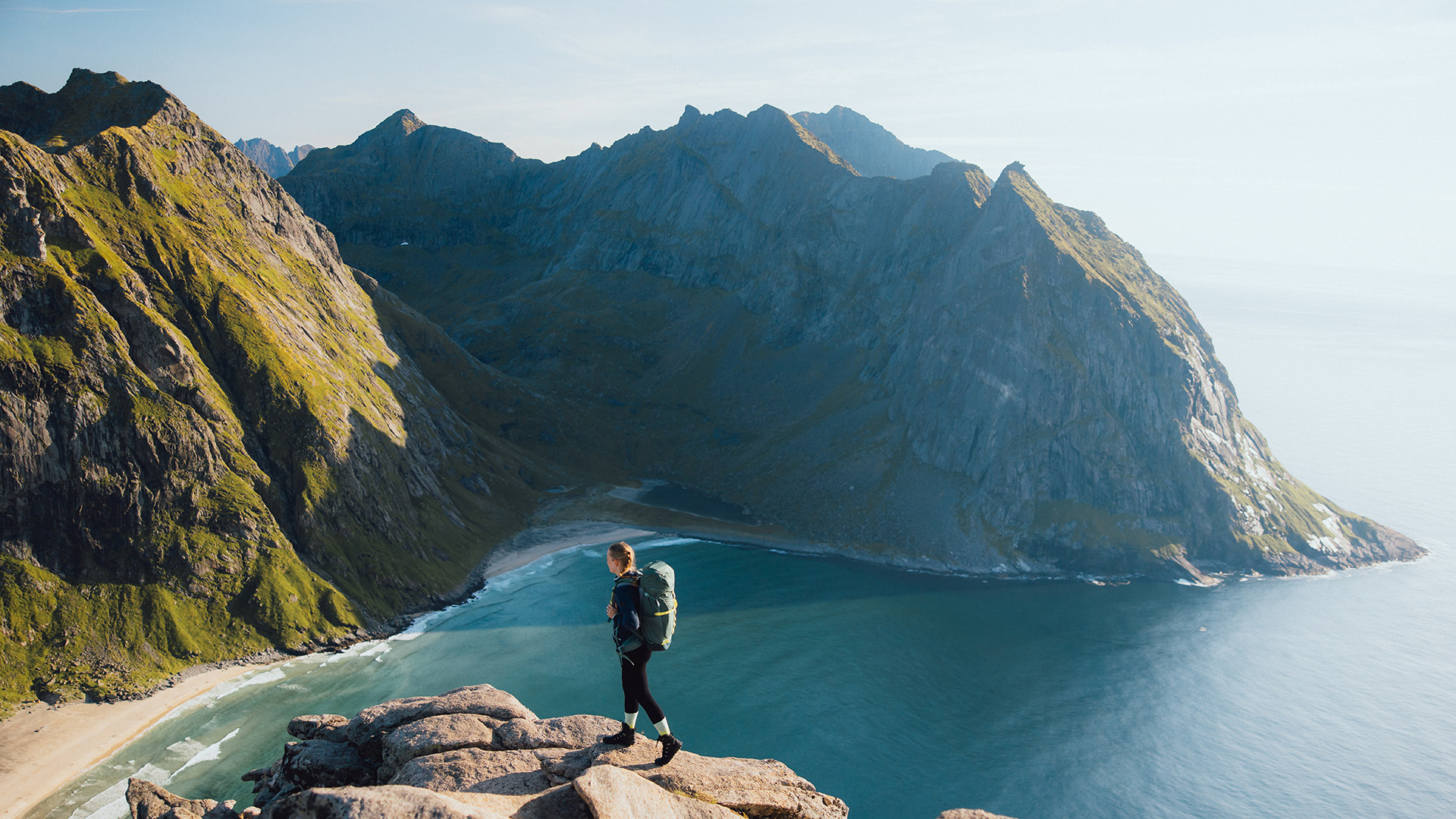 Wanderin mit Rucksack auf einem Berggipfel mit Blick auf das Meer und steile Felsen.