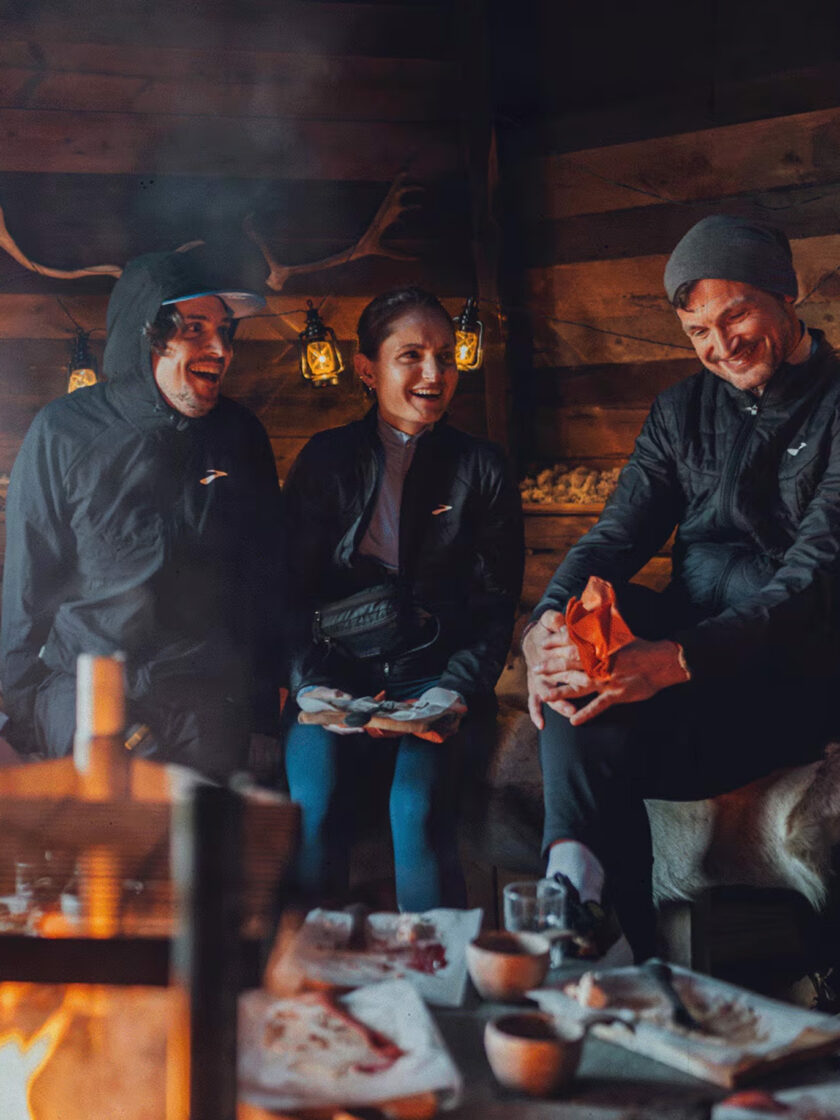 Gemütliche Runde am Kamin: Drei Freunde genießen Snacks in einer rustikalen Hütte.