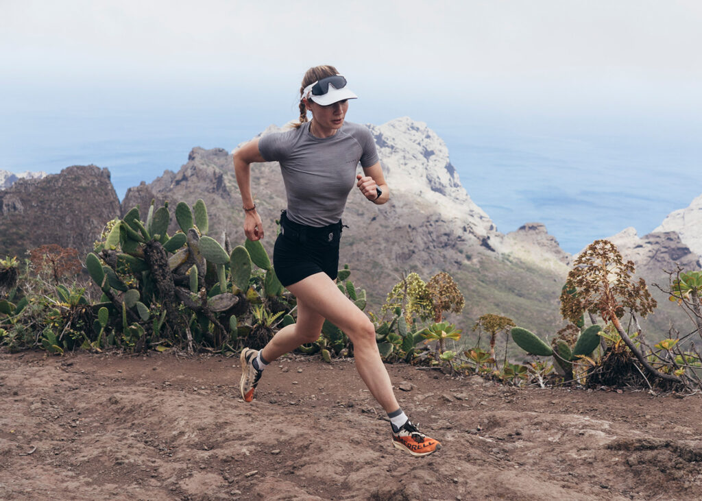 Frau in Sportkleidung läuft auf einem Bergpfad in Teneriffa mit Meerblick.