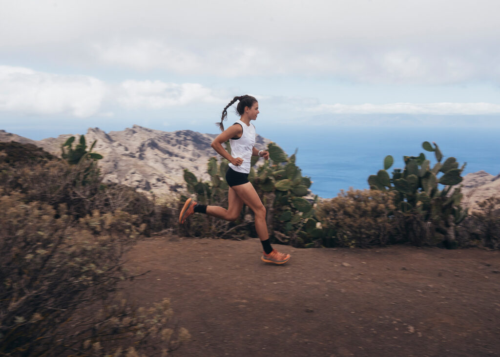 Frau in Sportkleidung läuft auf einem Bergpfad in Teneriffa mit Meerblick.