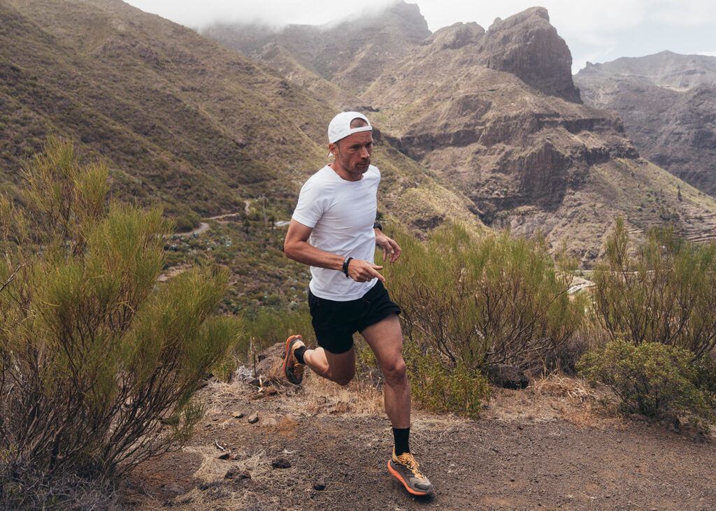 Mann in Sportkleidung läuft auf einem Bergpfad in Teneriffa, umgeben von wilder Natur.