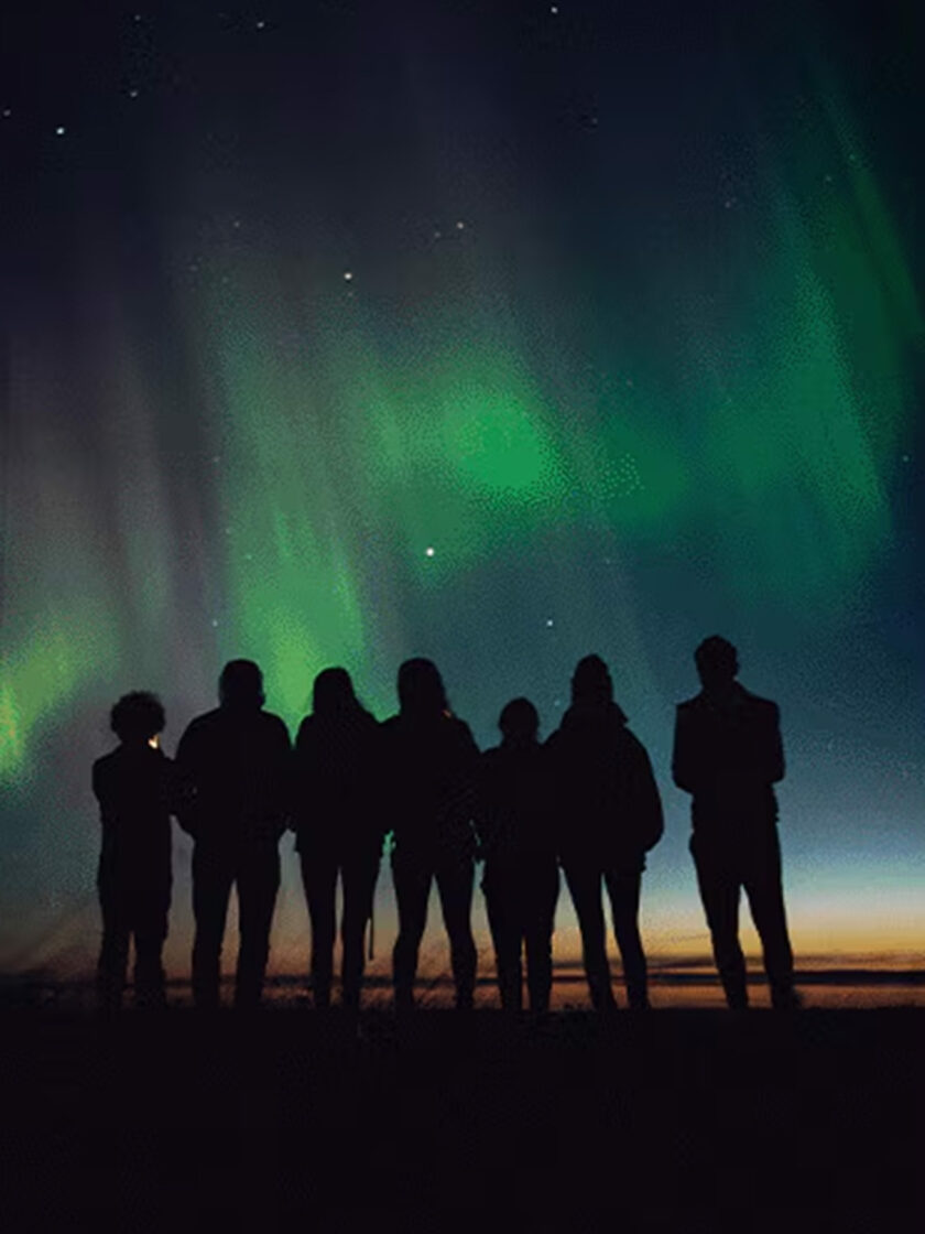 Silhouette von Menschen vor dem spektakulären Nordlicht am Nachthimmel.