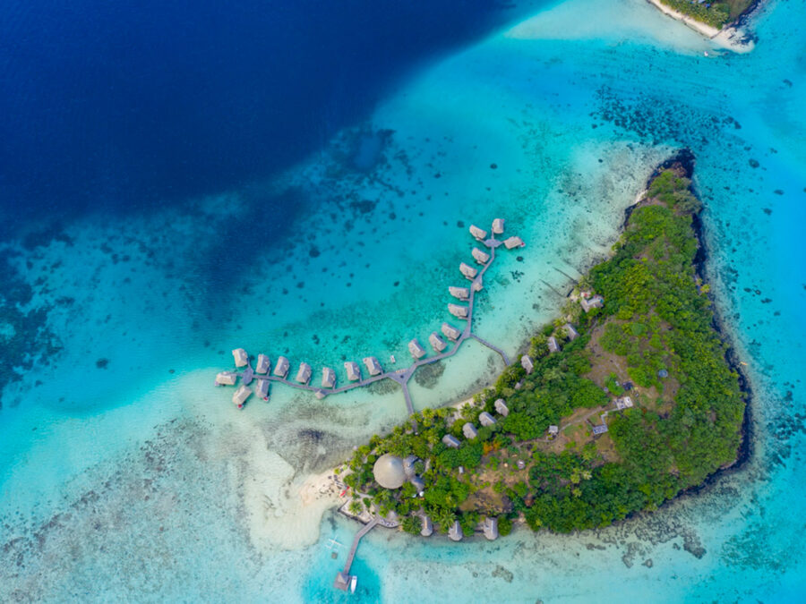 Tropisches Paradies: Luftaufnahme einer malerischen Insel mit Wasserbungalows und klarem, blauem Wasser.