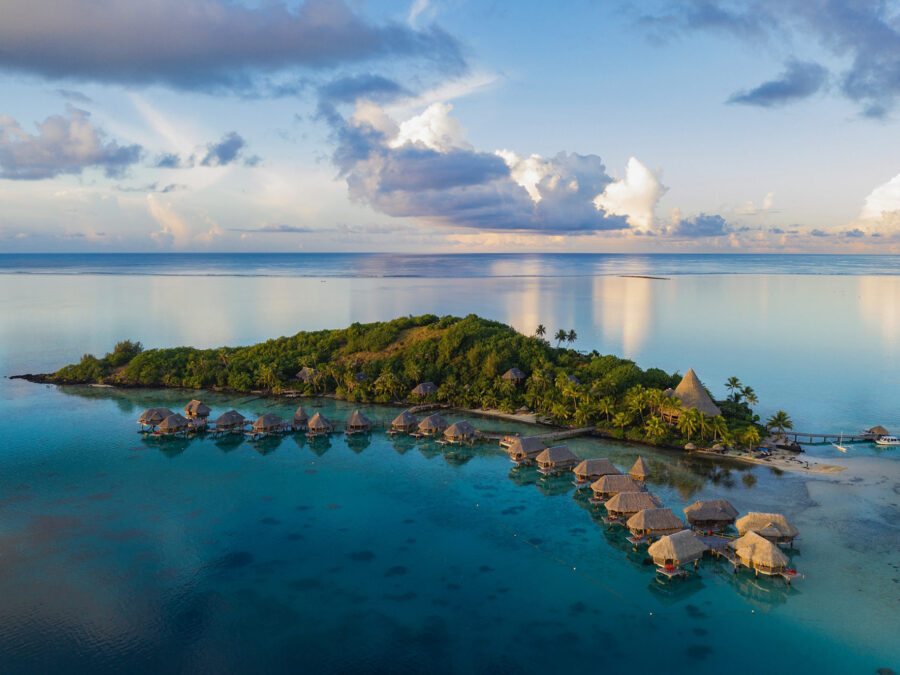 Tropische Insel mit über Wasser stehenden Bungalows und klarem, blauem Wasser.