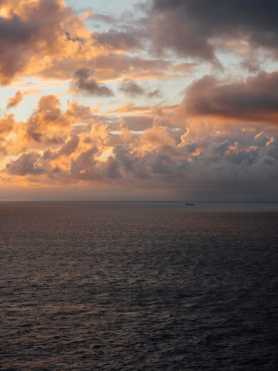 Ein Schiff in der Ferne auf dem ruhigen Meer unter einem Himmel mit dramatischen Wolken