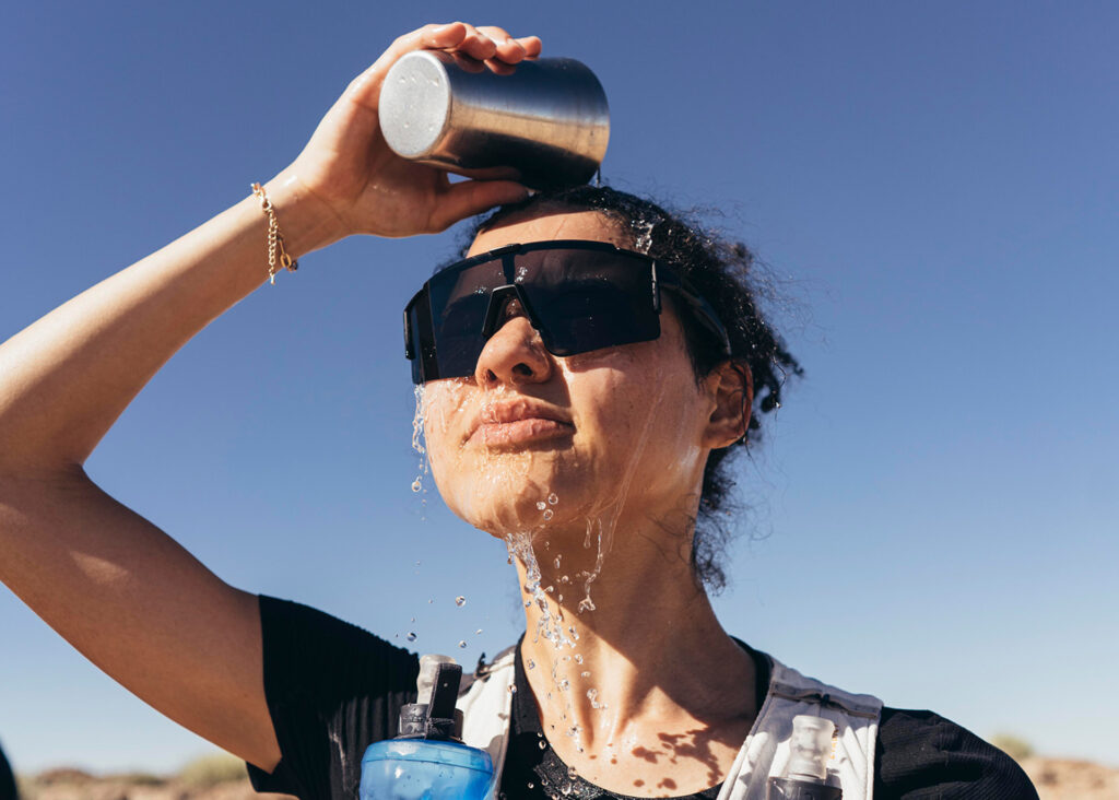 Frau mit Sonnenbrille kippt Wasser über ihren Kopf zur Erfrischung.