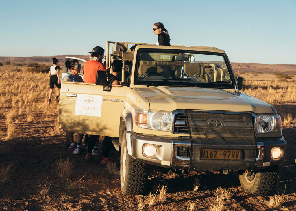 Safari-Teilnehmer steigen in einen offenen Geländewagen in der Wüste.