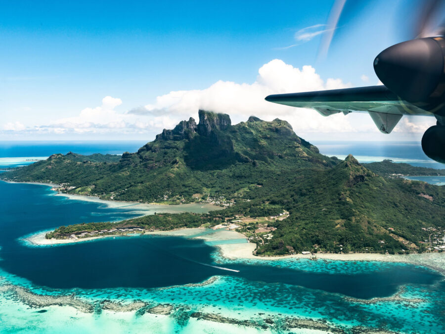 Luftaufnahme von Bora Bora mit türkisblauem Wasser und üppiger Berglandschaft.