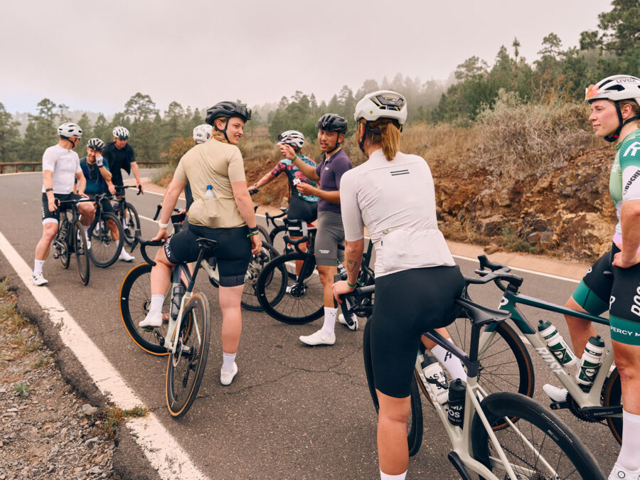 Gruppe von Radfahrern in sportlicher Kleidung diskutiert auf einer Landstraße in der Natur.