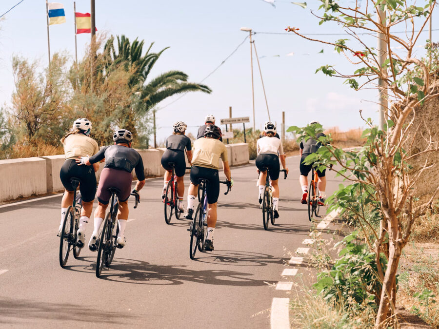 Gruppe von Radfahrern auf einer malerischen Straße mit Palmen und Flaggen.