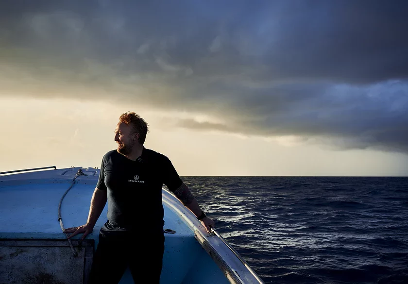 Mann steht auf einem Boot, blickt auf das offene Meer unter bewölktem Himmel.