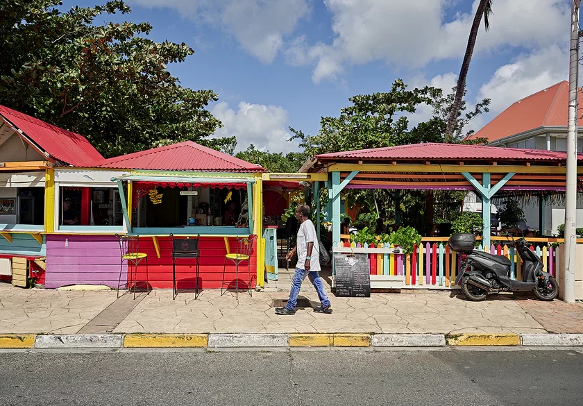 Bunte Strandrestaurants mit Palmen und einem Passanten auf der Straße.