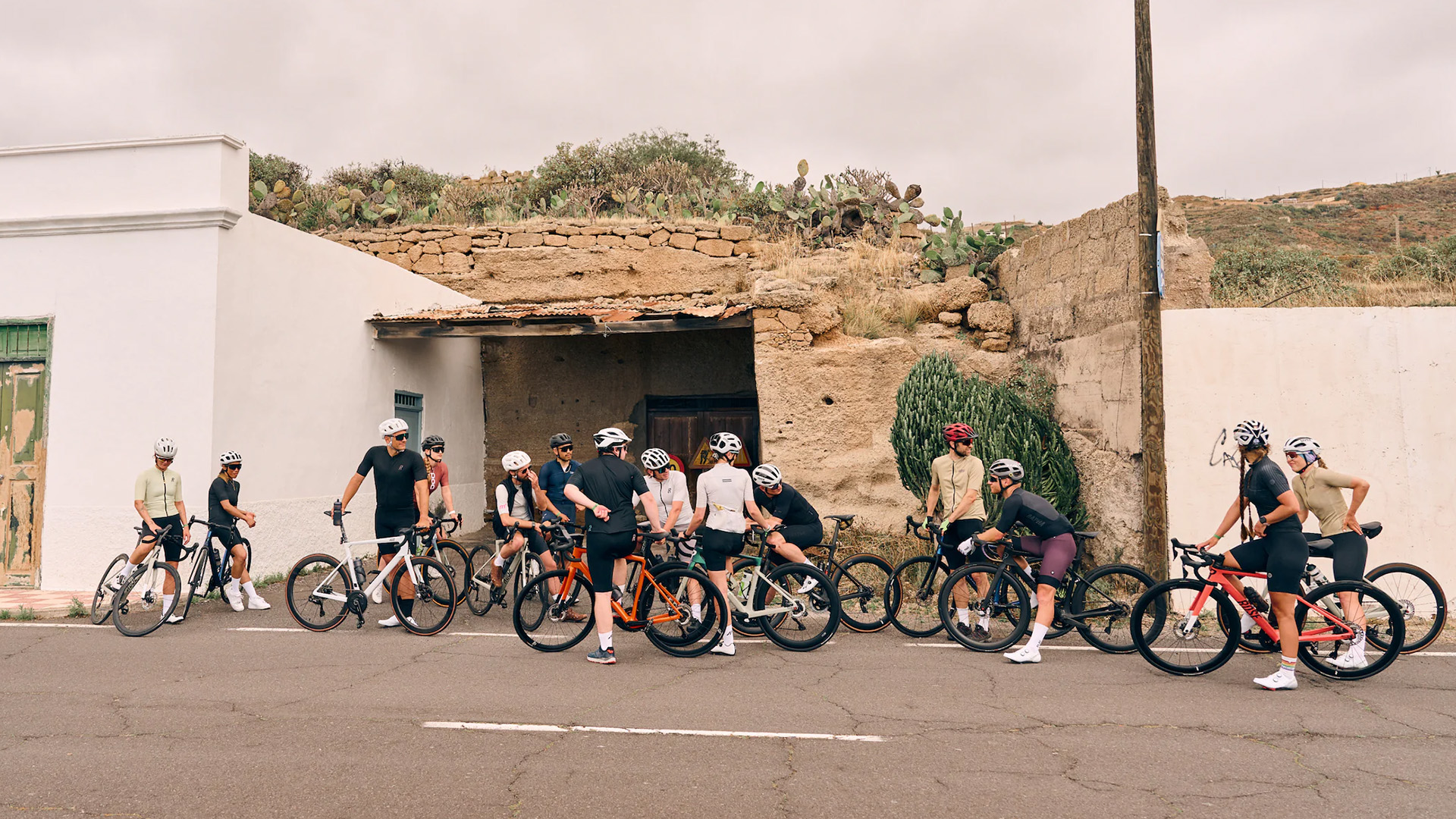 Gruppe von Radfahrern auf einer Straße vor historischen Gebäuden und Pflanzen.