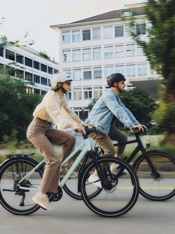 Zwei Radfahrer auf modernen E-Bikes in urbaner Umgebung unterwegs.